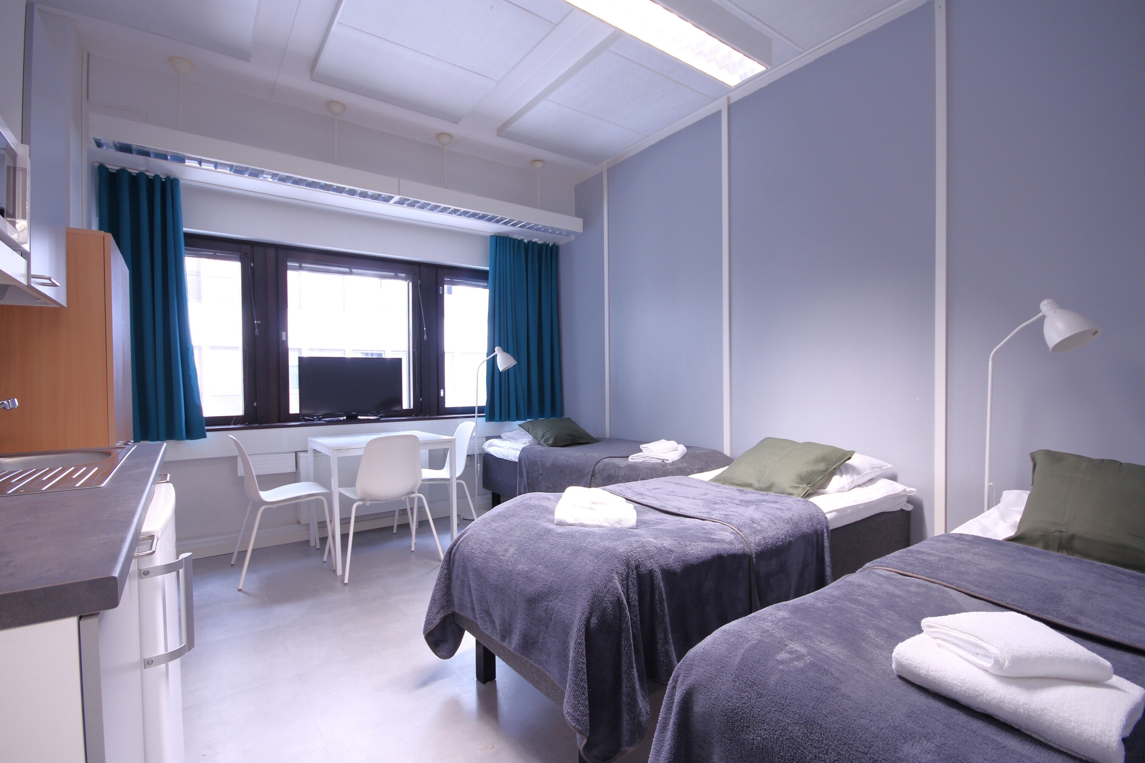 Una habitación de hotel con dos camas, un escritorio, una silla y una ventana con cortinas.
