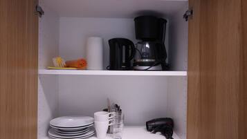 Une cuisine équipée d’une machine à café, d’assiettes, de tasses et d’un sèche-cheveux rangé sur les étagères.