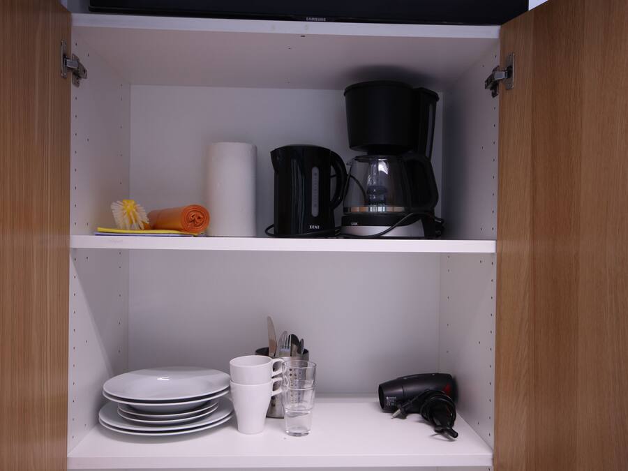 Une cuisine équipée d’une machine à café, d’assiettes, de tasses et d’un sèche-cheveux rangé sur les étagères.