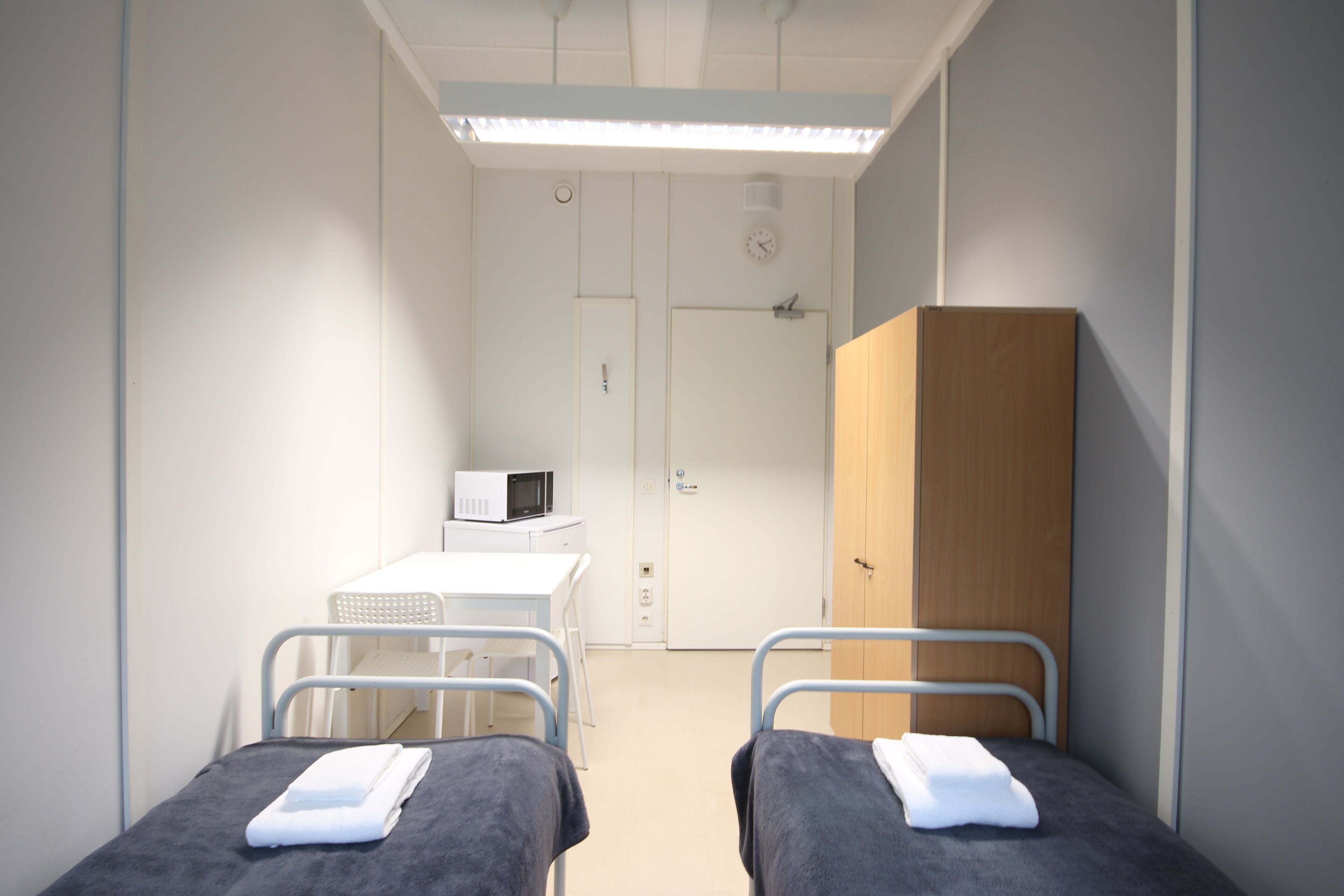 A hospital room with two beds, a white desk with a microwave, and a wooden cabinet.