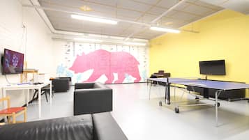 A room with a ping pong table, a sofa, a TV, and a wall with a bear mural.