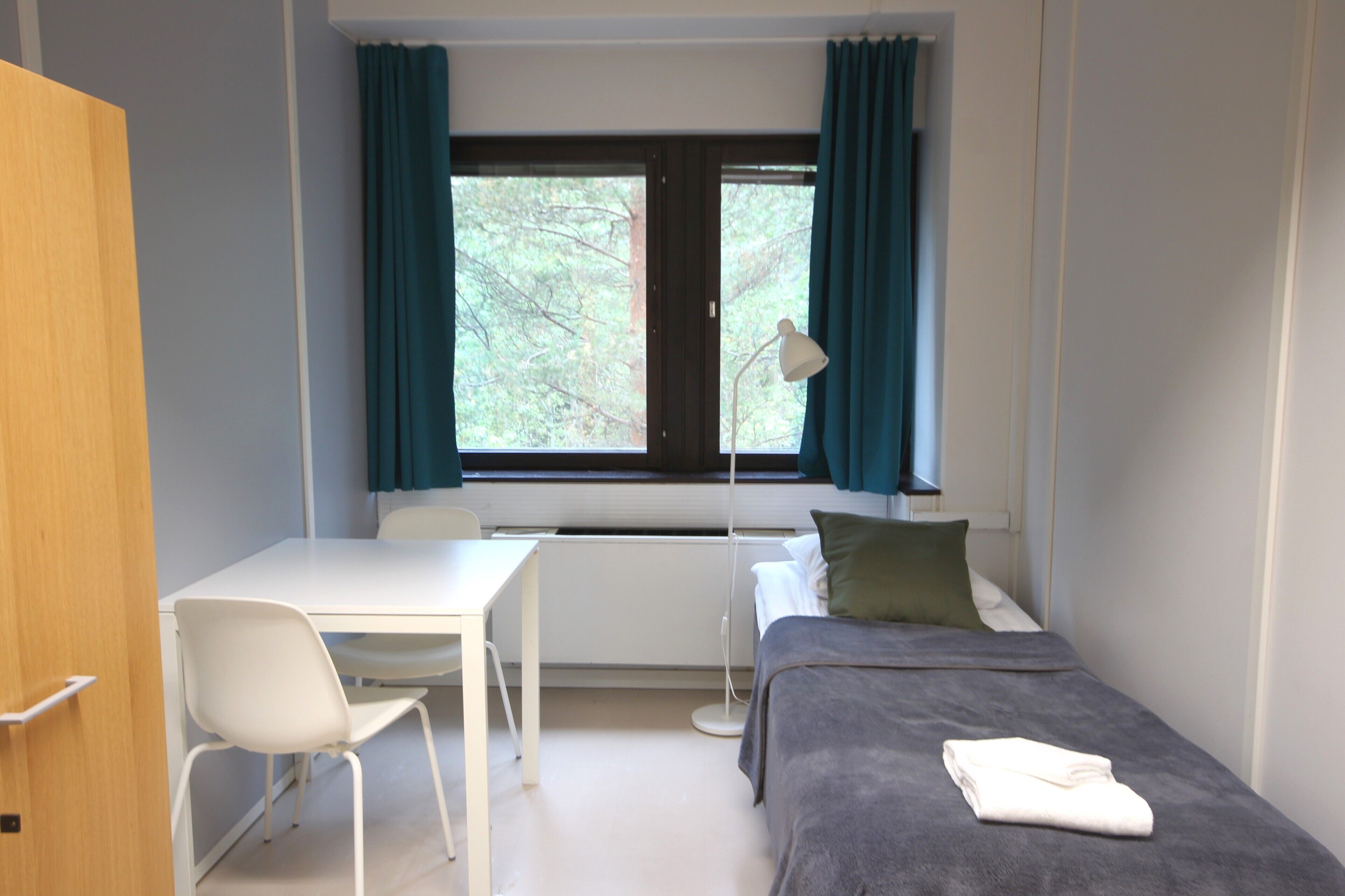 A room with a bed, a desk, a chair, a lamp, and a window with curtains.