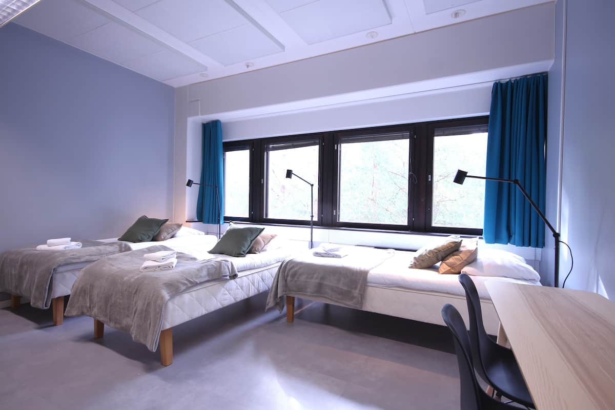 A room with two beds, a desk, and a window with curtains.