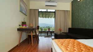 Ein Hotelzimmer mit einem Bett, einem Schreibtisch, einem Sessel, einem kleinen Tisch und einer Couch. Ein Fenster bietet einen Ausblick ins Freie.