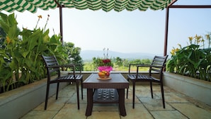 Eine Terrasse mit zwei Holzstühlen und einem Tisch, einem grün-weiß gestreiften Sonnenschirm und Blick auf entfernte Berge.