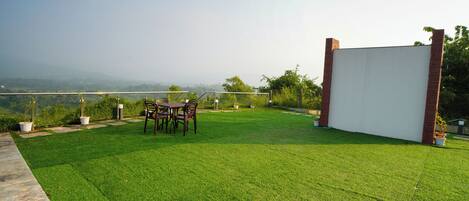 A well-maintained lawn with a patio table and chairs, surrounded by potted plants and a white structure.