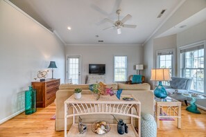A living room with a sofa, a television, a ceiling fan, and a window with blinds. - Port Folio - Adorable 3 BR home with Covered Porch! (Surf City)