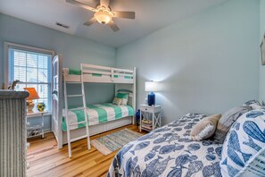 A bunk bed room with a ceiling fan, a bedside table with a lamp, and a window with blinds. - Port Folio - Adorable 3 BR home with Covered Porch! (Surf City)