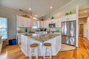 A modern kitchen with white cabinetry, a stainless steel refrigerator, and a granite island with stools. - Port Folio - Adorable 3 BR home with Covered Porch! (Surf City)