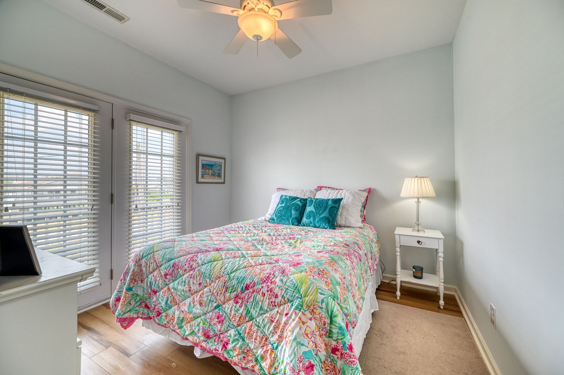 Une chambre à coucher avec un lit, une table de chevet, un ventilateur de plafond et une fenêtre avec des stores.