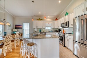 A modern kitchen with white cabinetry, stainless steel appliances, and a central island with bar stools. - Port Folio - Adorable 3 BR home with Covered Porch! (Surf City)