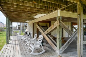 A covered outdoor seating area with wooden flooring and white rocking chairs.