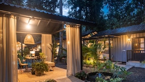 A covered outdoor seating area with a table and chairs, surrounded by potted plants and a small water feature. - KAÑIK APART HOTEL (Cahuita)