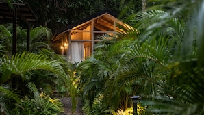 A wooden cabin surrounded by lush greenery, with a gravel path leading to it. - KAÑIK APART HOTEL (Cahuita)