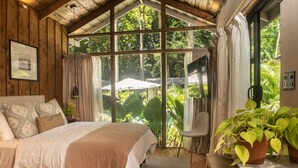 A cozy bedroom with a large window, a bed with patterned pillows, and a potted plant. - KAÑIK APART HOTEL (Cahuita)