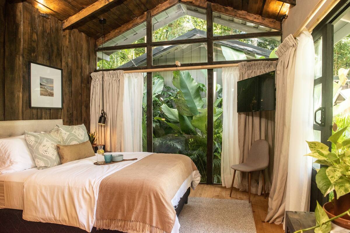 Un dormitorio con una cama grande, televisor y ventana con cortinas.