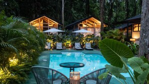 A pool area with lounge chairs and umbrellas, surrounded by tropical plants and wooden structures. - KAÑIK APART HOTEL (Cahuita)