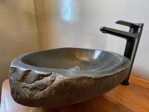 A stone sink with a modern faucet on a wooden surface.