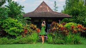 A person standing in front of a traditional thatched-roof structure surrounded by lush greenery. - Amartya Puri Green Cottages (Munduk)