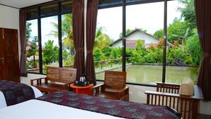 A hotel room with two beds, a small table with a kettle, and a view of a garden and water body outside. - Amartya Puri Green Cottages (Munduk)