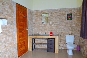 Un baño con pared de piedra, puerta de madera, lavabo, inodoro y espejo.