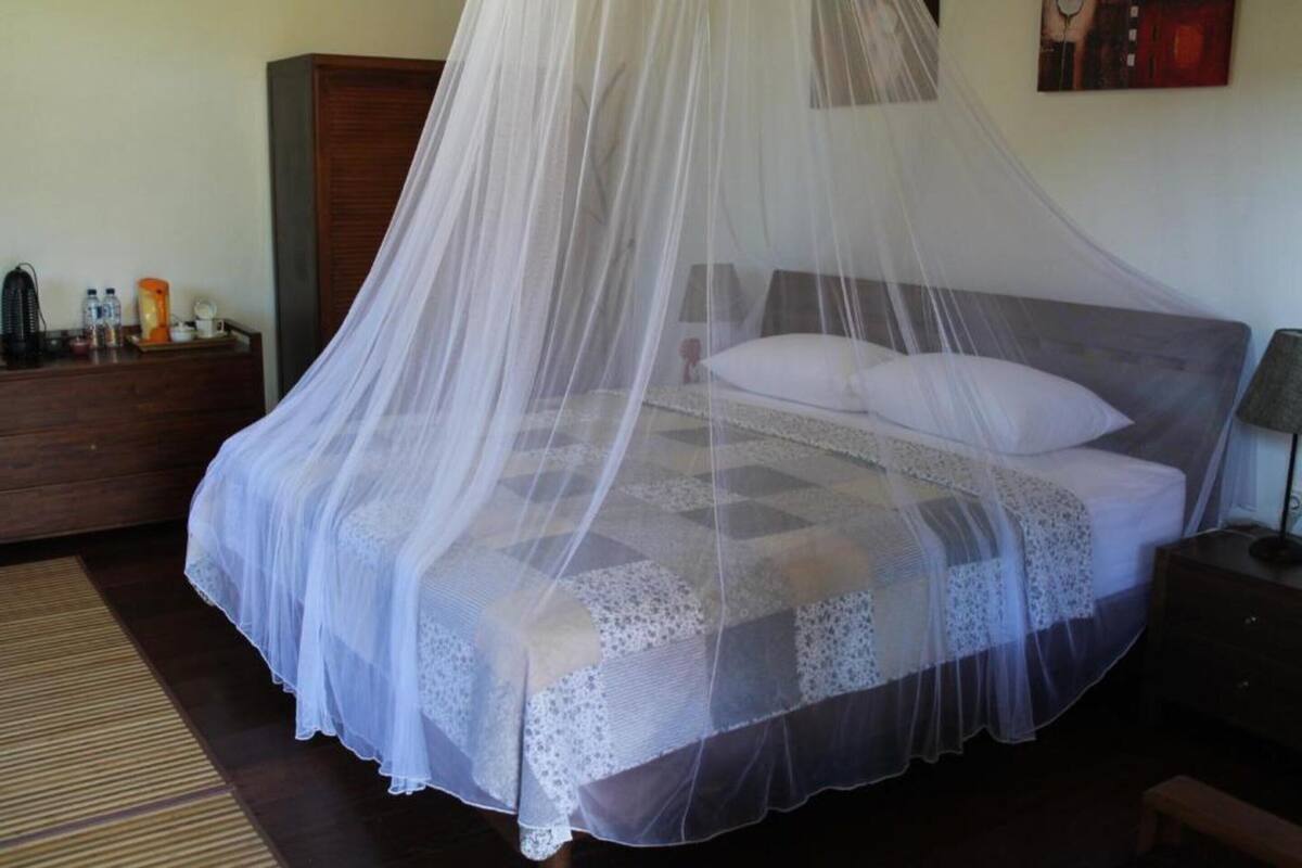 A bed with a white bedspread and lace trim, a wooden nightstand, a wooden wardrobe, and a bedside table with a lamp.
