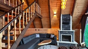 Een houten interieur met een trap, een open haard, een bank en een ronde tafel.