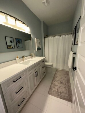A bathroom with a white sink, vanity, and toilet. There are framed pictures on the wall and a shower curtain. - Brand new riverfront luxurious townhome with Interior designer finishes.  (Melbourne)