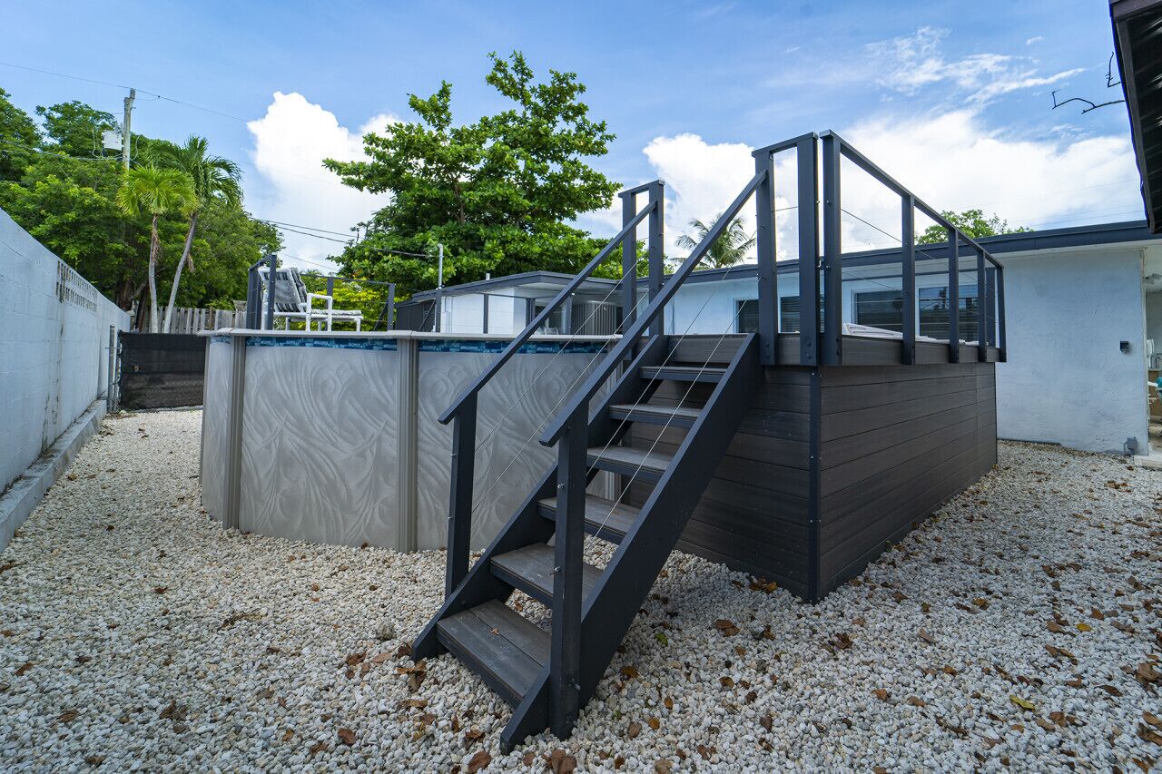 A modern outdoor staircase leading to a covered area with a view of a residential building and trees.