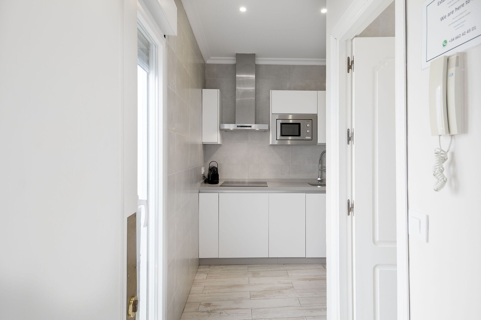 A narrow kitchen with white cabinets, a stainless steel microwave, and a stainless steel range hood.
