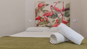 Hotellihuone, jossa on sänky, valkoiset vuodevaatteet, vihreä heittopeitto ja seinällä oleva flamingoaiheinen taulu.
