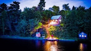 Una cabaña junto al lago con muelle, rodeada de un bosque denso.