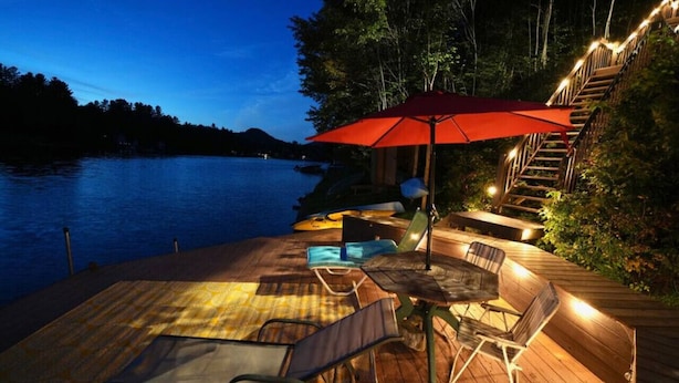 Una terraza de madera con mobiliario exterior, un paraguas rojo y una escalera que lleva a un nivel superior.