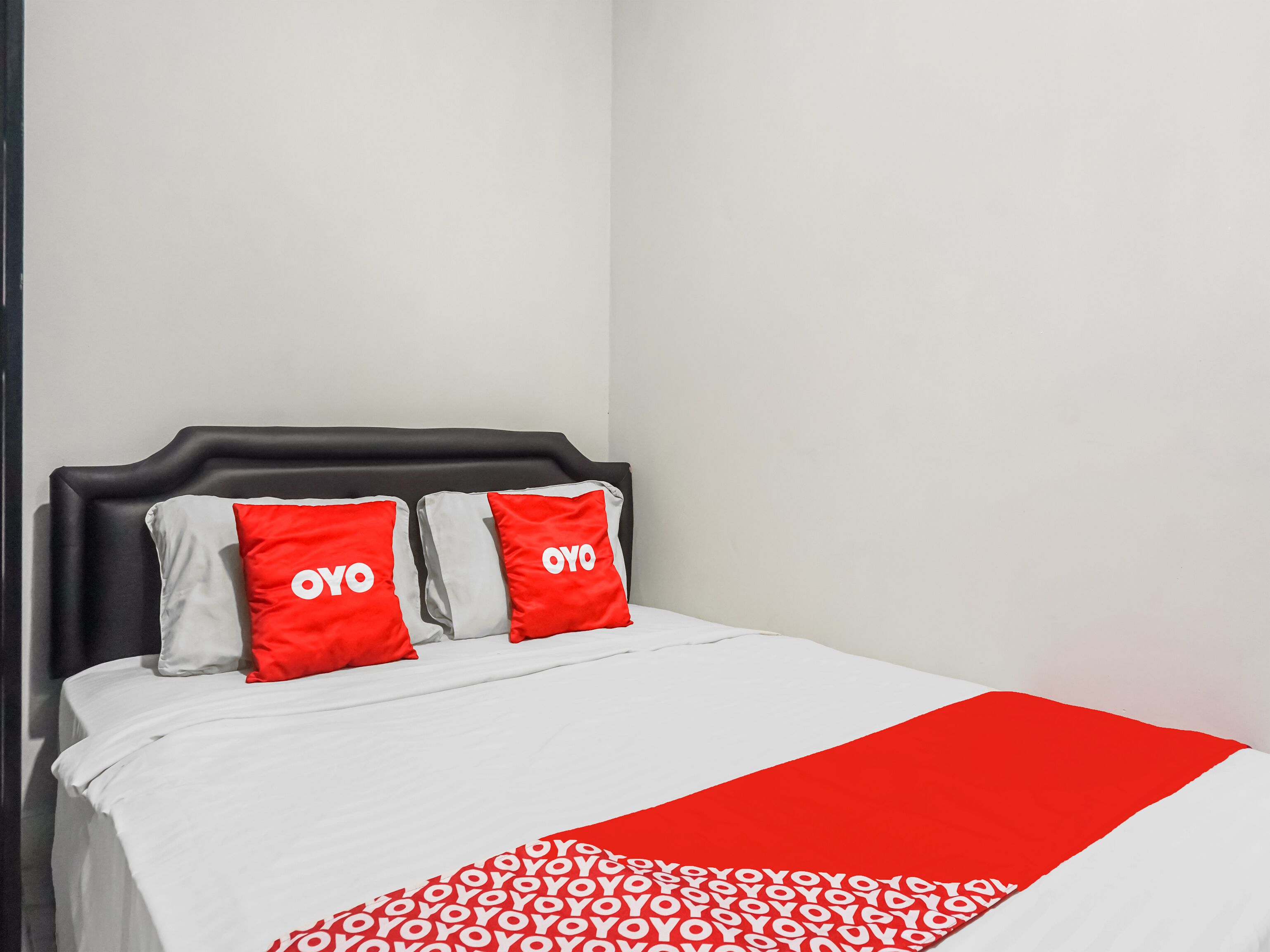 A bed with a white and red bedspread, two pillows with "OYO" branding, and a red blanket.