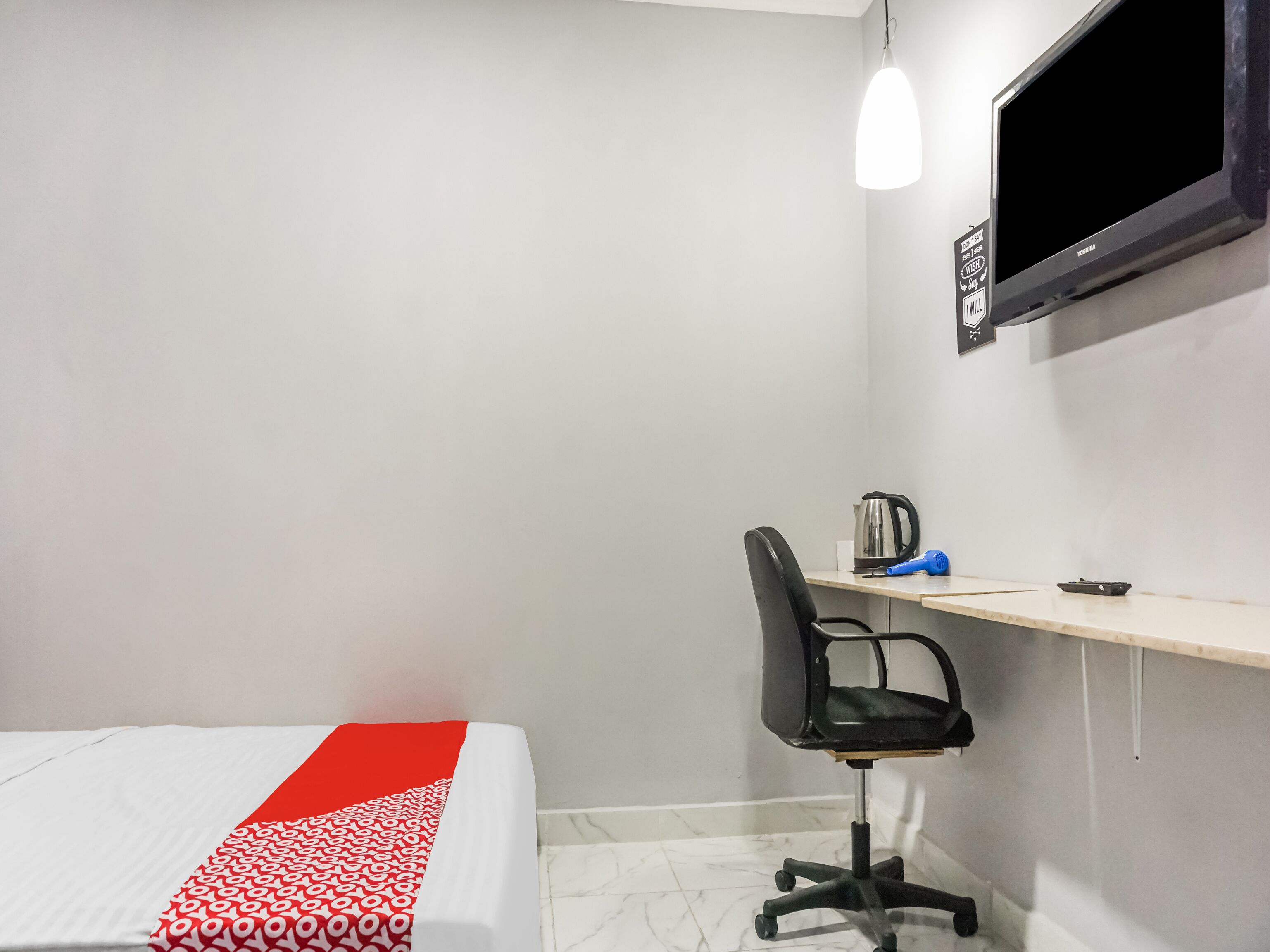 Una habitación de hotel con cama, escritorio, silla, televisor y hervidor.