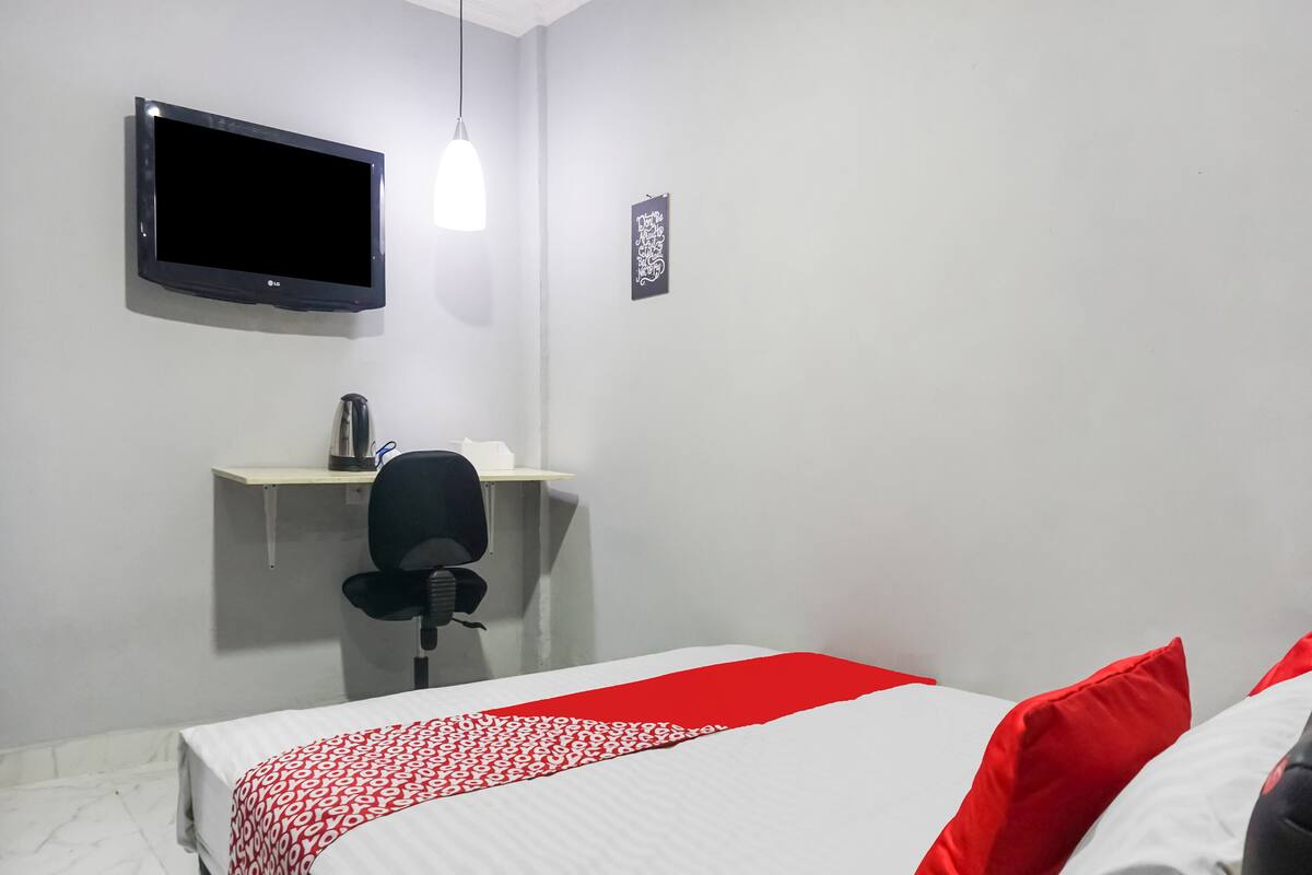 A hotel room with a bed, a desk with a chair, a television, and a shelf.