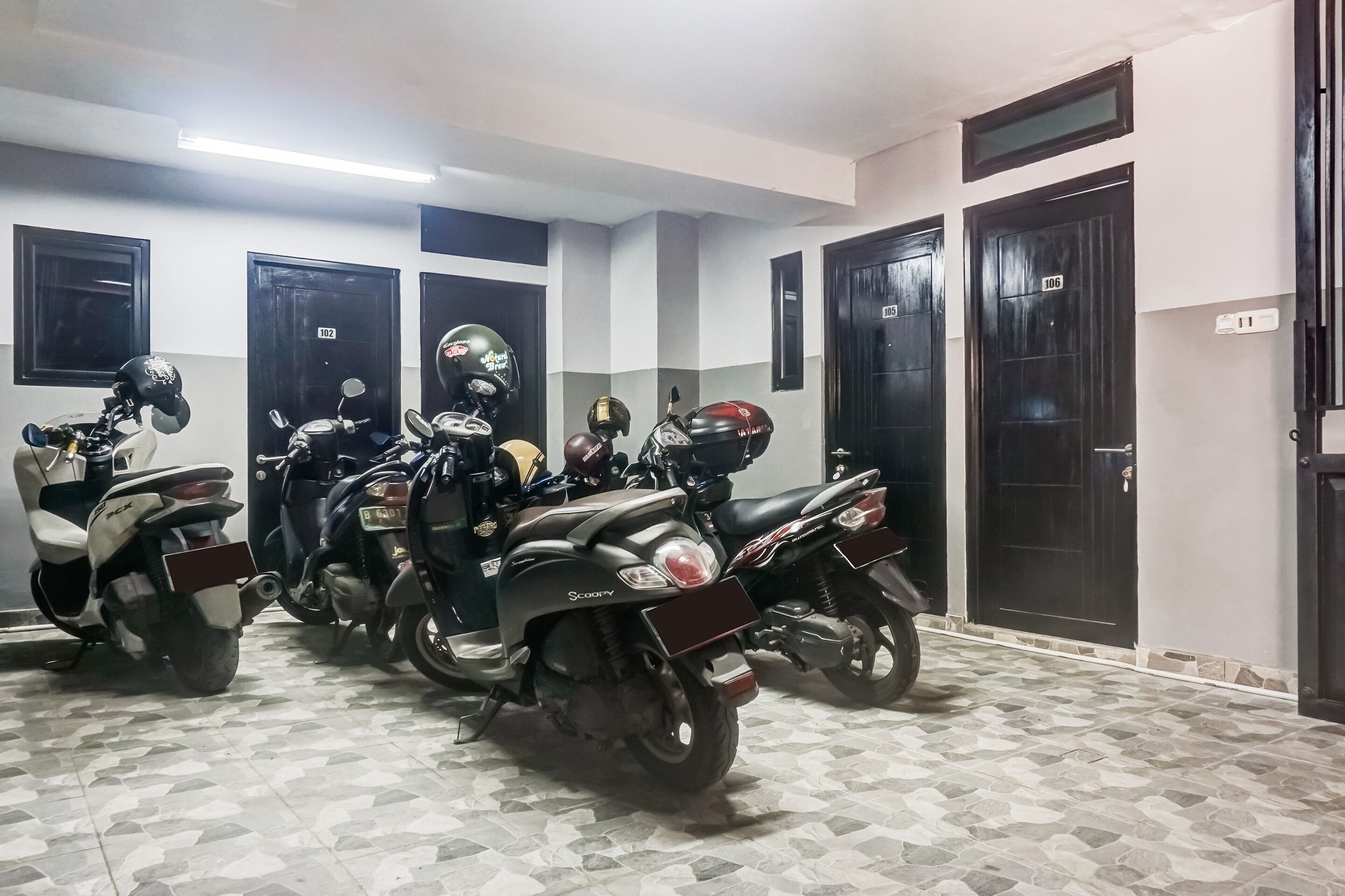 Varias motocicletas estacionadas en una habitación con puertas numeradas y piso de baldosas.