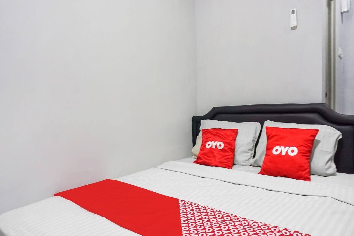A bed with a white and red bedspread, two red pillows with "OYO" text, and a black headboard.