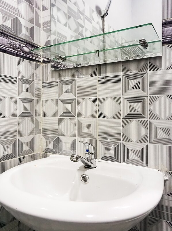 A bathroom with a white sink, a glass shelf above it, and patterned tiles on the walls. - Collection O 91131 New V1 Hotel Near Stasiun Mangga Besar (Jakarta)