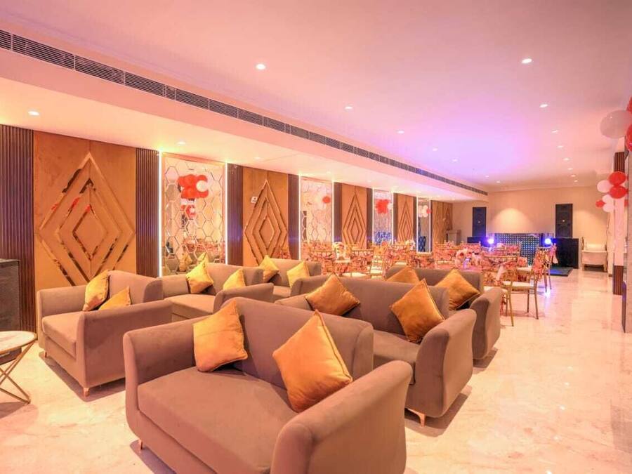 A spacious hotel lobby with sofas and tables, a stage for events, and a decorative wall with geometric patterns.