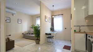 A compact living space with a sofa, a dining table, a potted plant, and a kitchen area including a washing machine. - Tejares 16, Apartment 2 bedrooms Ground Floor (Sevilla)