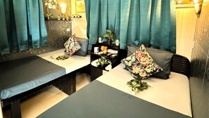 A spa room with two beds, teal curtains, a wall-mounted lamp, a shelf with toiletries, and a small plant. - Park Guest House (Kowloon)
