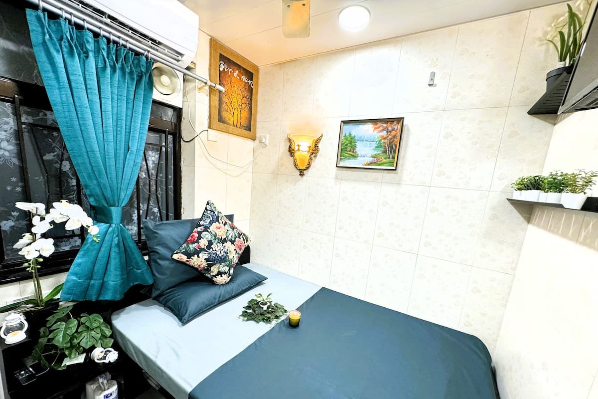 A neatly arranged bedroom with a bed, a window with curtains, a wall-mounted shelf with plants, and a painting.