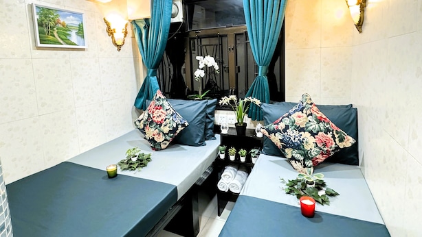 A room with two beds, teal curtains, wall-mounted lights, a small table with a plant, and a painting on the wall. - Park Guest House (Kowloon)