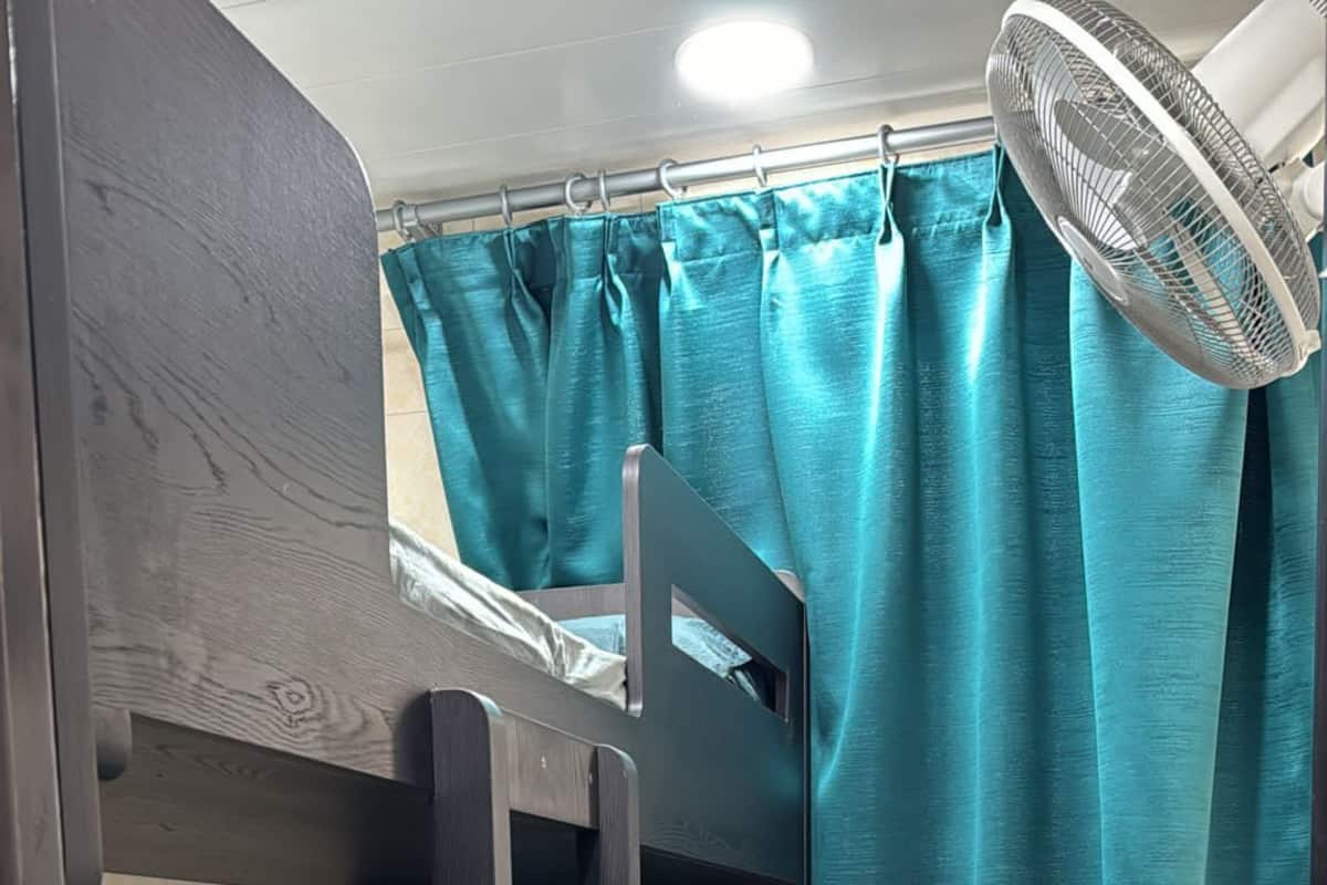 A compact room with bunk beds, a small desk, a fan, and a curtain.