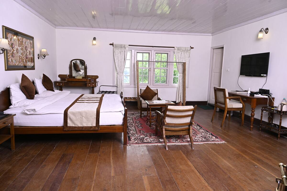 A bedroom with a large bed, a desk, a chair, a TV, and a window with curtains.