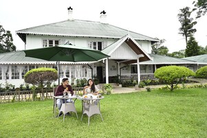 A two-story house with a porch and a dining area with two tables and chairs.