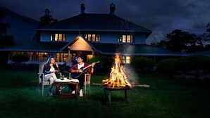 Ein Haus mit großem Vorgarten, Feuerstelle und Essplatz mit Stühlen.