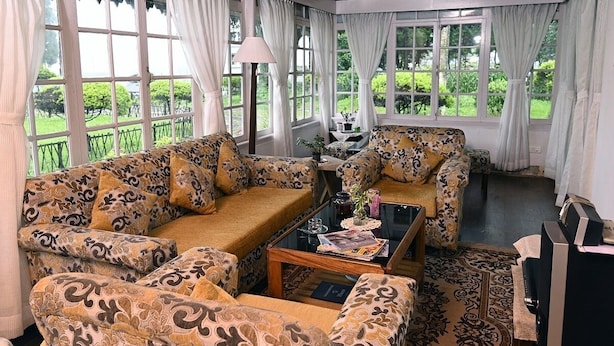 Ein gemütliches Wohnzimmer mit gemusterten Sofas, einem Couchtisch und großen Fenstern mit Blick auf einen Garten.