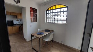Une cuisine compacte avec des meubles en bois et un réfrigérateur noir. Un coin repas, composé d’une table et de deux chaises, est situé à côté de la cuisine.